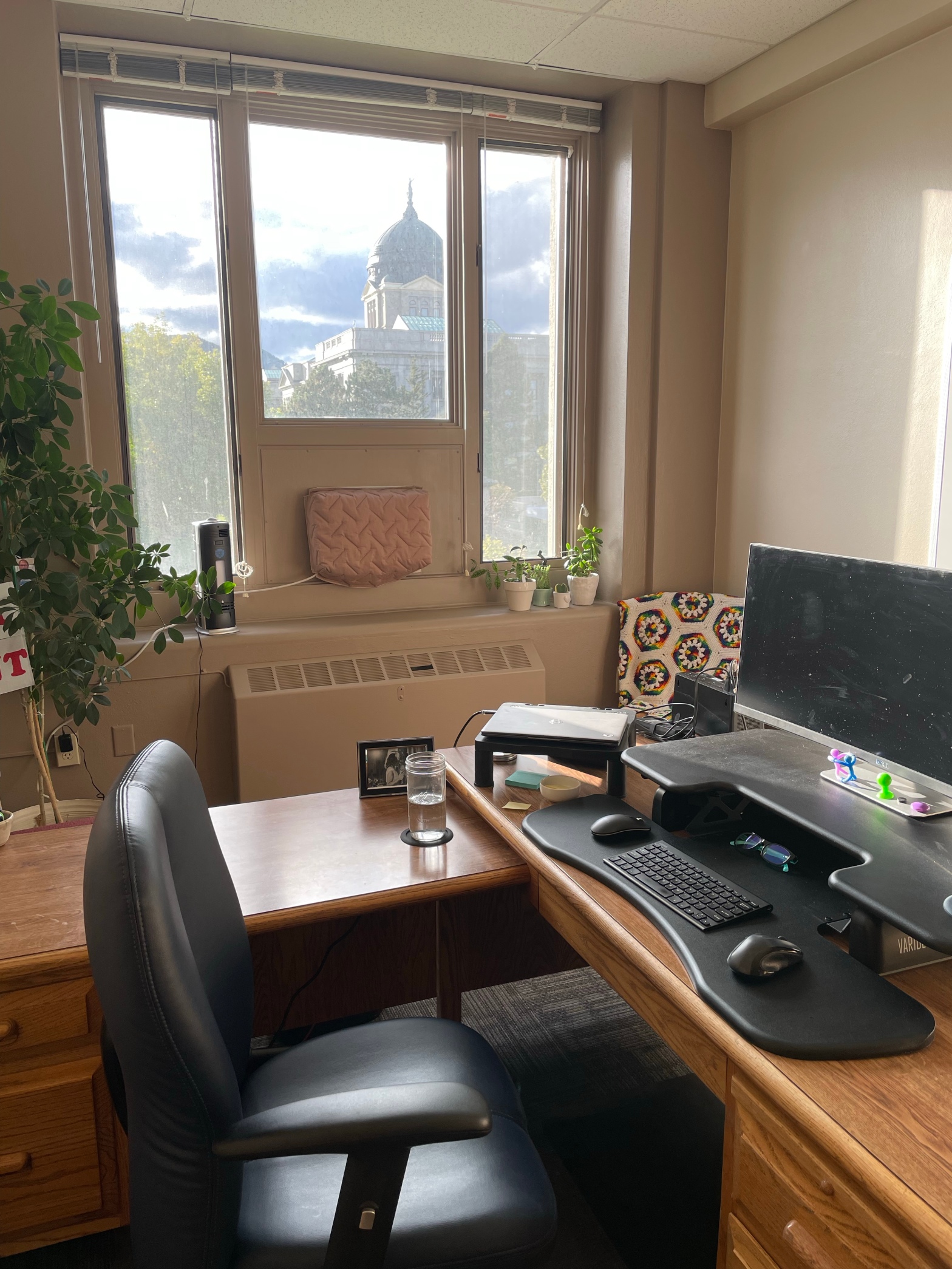 wooden desk with a large monitor in the foreground with a view out the window of a government building in the background